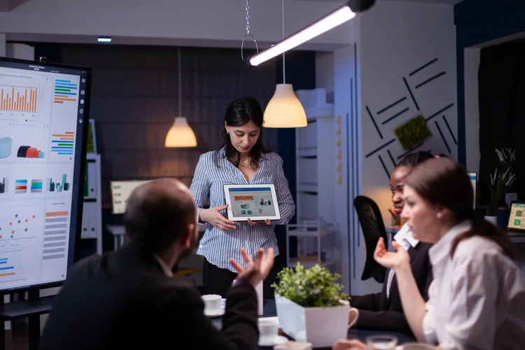 Profissionais de marketing têm salários que variam de R$ 2 mil a mais de R$ 85 mil por mês 1 mulher empreendedora workaholic sobrecarregada de trabalho exibindo graficos de marketing usando tablet trabalhando demais na solucao da empresa tarde da noite na sala de reunioes